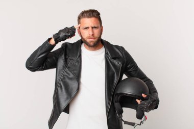 Genç yakışıklı adam kafası karışık ve şaşkın hissediyor, deli olduğunu gösteriyor. Motosiklet kaskı konsepti