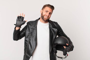 Genç yakışıklı adam mutlu bir şekilde gülümsüyor, el sallıyor, sizi selamlıyor ve selamlıyor. Motosiklet kaskı konsepti