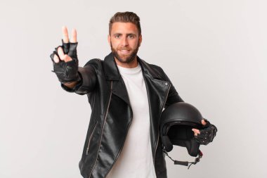 Genç yakışıklı adam gülümsüyor ve arkadaş canlısı görünüyor, iki numarayı gösteriyor. Motosiklet kaskı konsepti