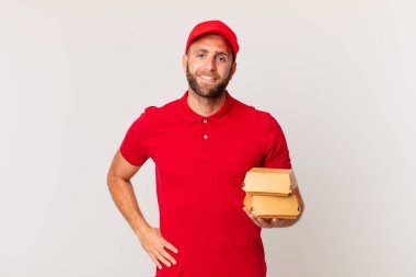 young handsome man smiling happily with a hand on hip and confident burger delivering concept