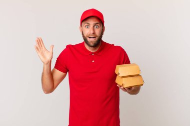 young handsome man feeling happy and astonished at something unbelievable burger delivering concept