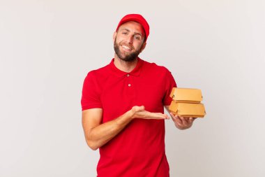young handsome man smiling cheerfully, feeling happy and showing a concept burger delivering concept