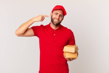 young handsome man smiling confidently pointing to own broad smile burger delivering concept