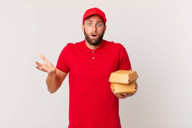 young handsome man amazed, shocked and astonished with an unbelievable surprise burger delivering concept