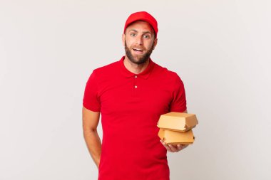 young handsome man looking happy and pleasantly surprised burger delivering concept