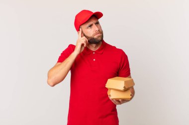 young handsome man thinking, feeling doubtful and confused burger delivering concept