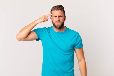 Genç yakışıklı adam kafası karışık ve şaşkın hissediyor, deli olduğunu gösteriyor. fitness konsepti