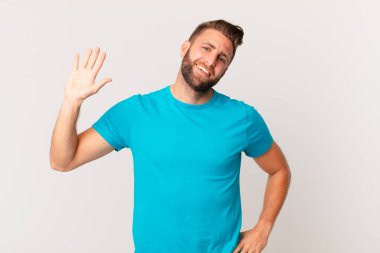 Genç yakışıklı adam mutlu bir şekilde gülümsüyor, el sallıyor, sizi selamlıyor ve selamlıyor. fitness konsepti