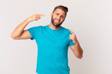 Genç ve yakışıklı bir adam kendi gülüşünü işaret ederek kendine güvenerek gülümsüyor. fitness konsepti