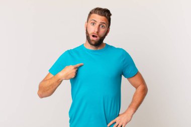 young handsome man looking shocked and surprised with mouth wide open, pointing to self. fitness concept