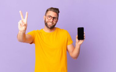 young handsome man smiling and looking happy, gesturing victory or peace. cell concept