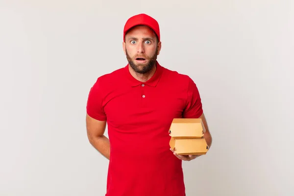 Young Handsome Man Looking Very Shocked Surprised Burger Delivering Concept — Stok fotoğraf