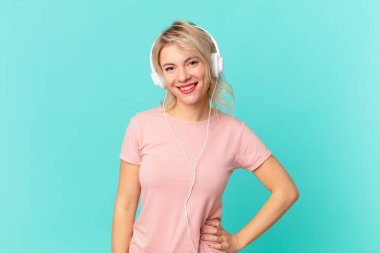 young pretty woman smiling happily with a hand on hip and confident. listening music concept