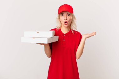 young pretty woman looking surprised and shocked, with jaw dropped holding an object. pizza delivering concept