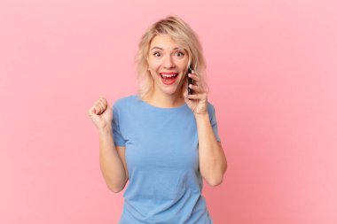 young pretty woman feeling shocked,laughing and celebrating success. cell concept