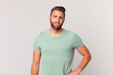 Genç yakışıklı adam mutlu bir şekilde gülümsüyor, eli kalçasında ve kendinden emin.