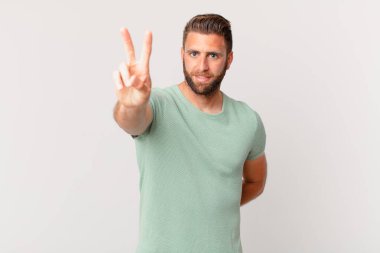 Genç yakışıklı adam gülümsüyor ve mutlu görünüyor, zafer ya da barış işareti yapıyor.