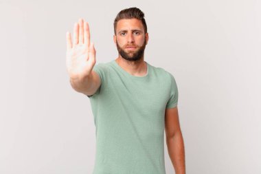 Genç ve yakışıklı adam ciddi görünüyor. Avuç içi gösteriyor. Durdurma hareketi yapıyor.
