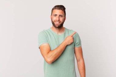 Genç yakışıklı adam neşeyle gülümsüyor, mutlu hissediyor ve bir tarafı işaret ediyor.