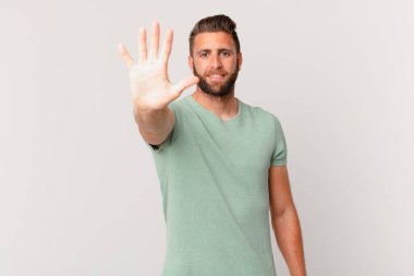 Genç yakışıklı adam gülümsüyor ve arkadaş canlısı görünüyor, beş numarayı gösteriyor.