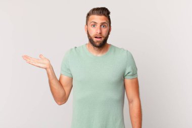 Genç yakışıklı adam şaşırmış ve şok olmuş görünüyor, çenesi düşmüş bir nesne tutuyor.