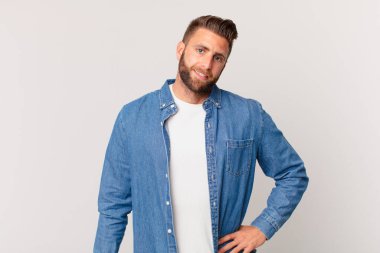 Genç yakışıklı adam mutlu bir şekilde gülümsüyor, eli kalçasında ve kendinden emin.