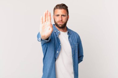 Genç ve yakışıklı adam ciddi görünüyor. Avuç içi gösteriyor. Durdurma hareketi yapıyor.