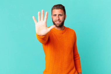 Genç yakışıklı adam gülümsüyor ve arkadaş canlısı görünüyor, beş numarayı gösteriyor.