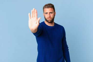 Genç ve yakışıklı adam ciddi görünüyor. Avuç içi gösteriyor. Durdurma hareketi yapıyor.