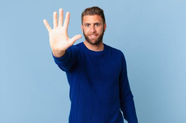 Genç yakışıklı adam gülümsüyor ve arkadaş canlısı görünüyor, beş numarayı gösteriyor.