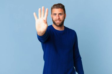 Genç yakışıklı adam gülümsüyor ve arkadaş canlısı görünüyor, dört numarayı gösteriyor.