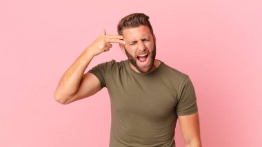 Genç yakışıklı adam mutsuz ve stresli görünüyor, intihar jesti silah işareti yapıyor.