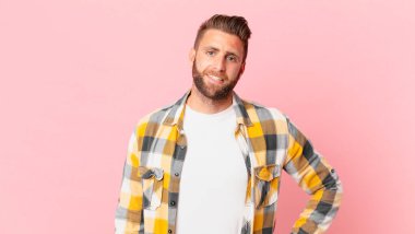 Genç yakışıklı adam mutlu bir şekilde gülümsüyor, eli kalçasında ve kendinden emin.