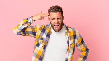 Genç yakışıklı adam mutsuz ve stresli görünüyor, intihar jesti silah işareti yapıyor.