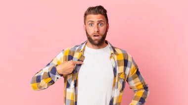 Şok olmuş ve ağzı açık, kendini işaret eden genç yakışıklı bir adam.