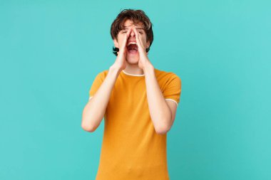 Genç yakışıklı adam mutlu hissediyor, elleri ağızda bağırıyor.