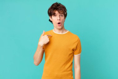 Şok olmuş ve ağzı açık, kendini işaret eden genç yakışıklı bir adam.