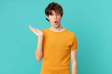 Genç yakışıklı adam şaşırmış ve şok olmuş görünüyor, çenesi düşmüş bir nesne tutuyor.