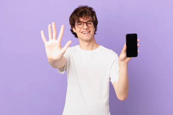 Young Man Smiling Looking Friendly Showing Number Five Holding Cell — Stockfoto