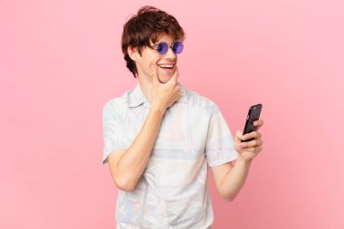 Cep telefonlu genç adam mutlu, kendinden emin bir ifadeyle gülümsüyor.