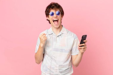 Cep telefonlu genç adam şok olmuş hissediyor, gülüyor ve başarıyı kutluyor.