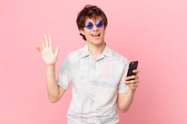 Cep telefonlu genç adam mutlu bir şekilde gülümsüyor, el sallıyor, seni selamlıyor ve selamlıyor.