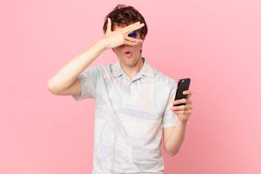 Cep telefonlu genç adam şok olmuş, korkmuş ya da korkmuş görünüyor.