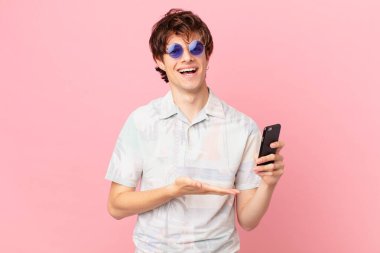 Cep telefonlu genç adam neşeli bir şekilde gülümsüyor, mutlu hissediyor ve bir konsept gösteriyor.