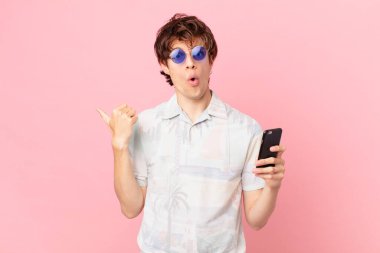 Cep telefonu olan genç bir adam inanamadığı için hayrete düşmüş görünüyor.