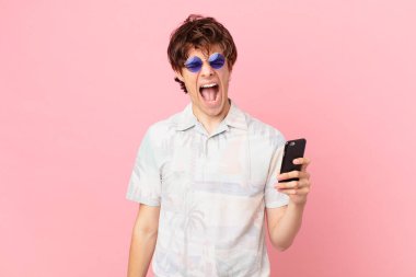 Cep telefonlu genç adam agresif bir şekilde bağırıyor, çok sinirli görünüyor.