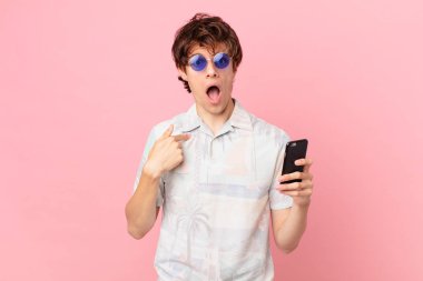 Cep telefonlu genç adam şok olmuş ve şaşırmış görünüyor, ağzı açık, kendini işaret ediyor.