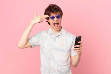 Cep telefonlu genç adam mutsuz ve stresli görünüyor, intihar jesti silah işareti yapıyor