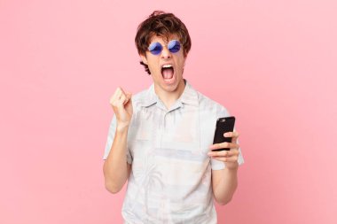 Cep telefonlu genç adam sinirli bir ifadeyle agresif bir şekilde bağırıyor.