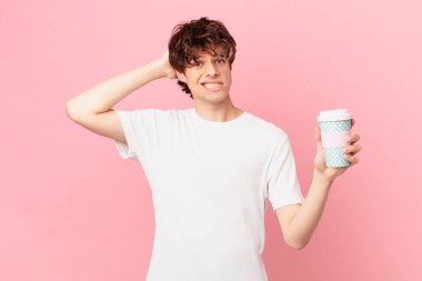 Elinde kahve olan genç adam stresli, endişeli ya da korkmuş, elleri başının üstünde.